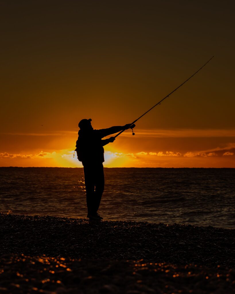 A serene scene of a man casting his fishing rod against a vibrant sunset over the ocean.