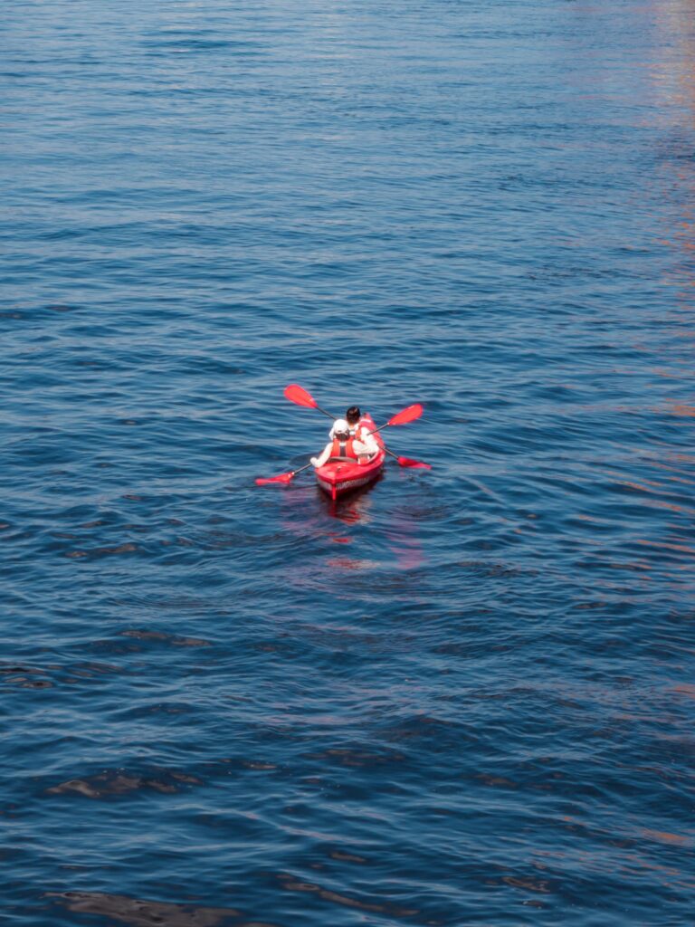 Red kayak with paddlers on calm blue waters in Trondheim, Norway.