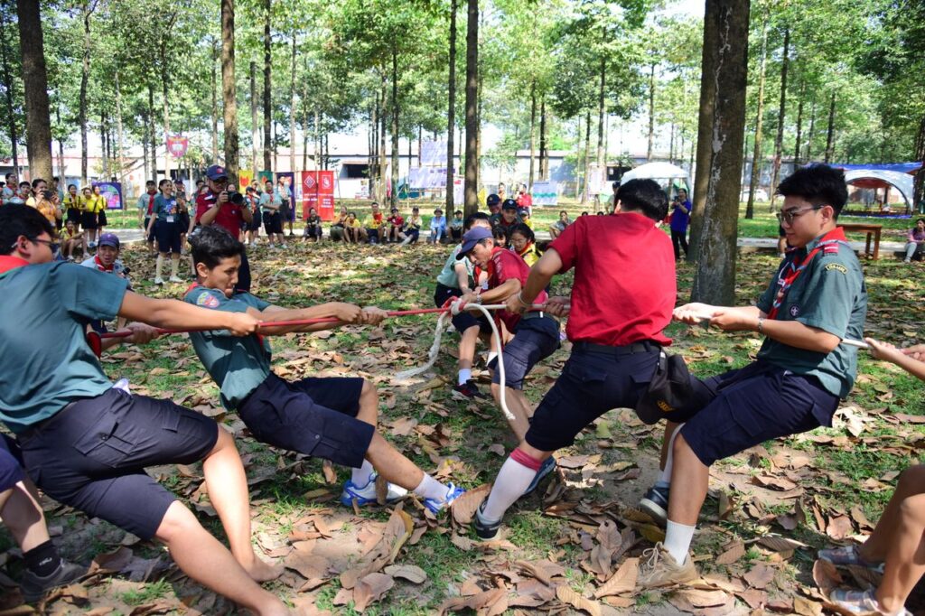 Scouts engaged in a vigorous outdoor tug-of-war game in a sunlit forest setting.